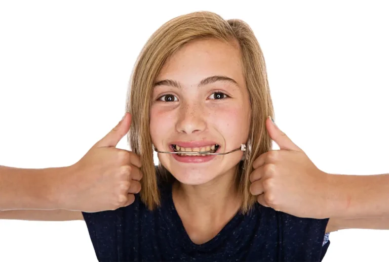 Smiling child with straight, shoulder-length hair wearing orthodontic headgear and giving two thumbs up at a Superhero Dress Up Day during Muir Station Smiles events.